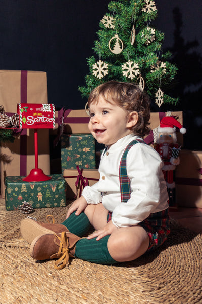 Child sitting on the floor with a Christmas tree and presents in the background
